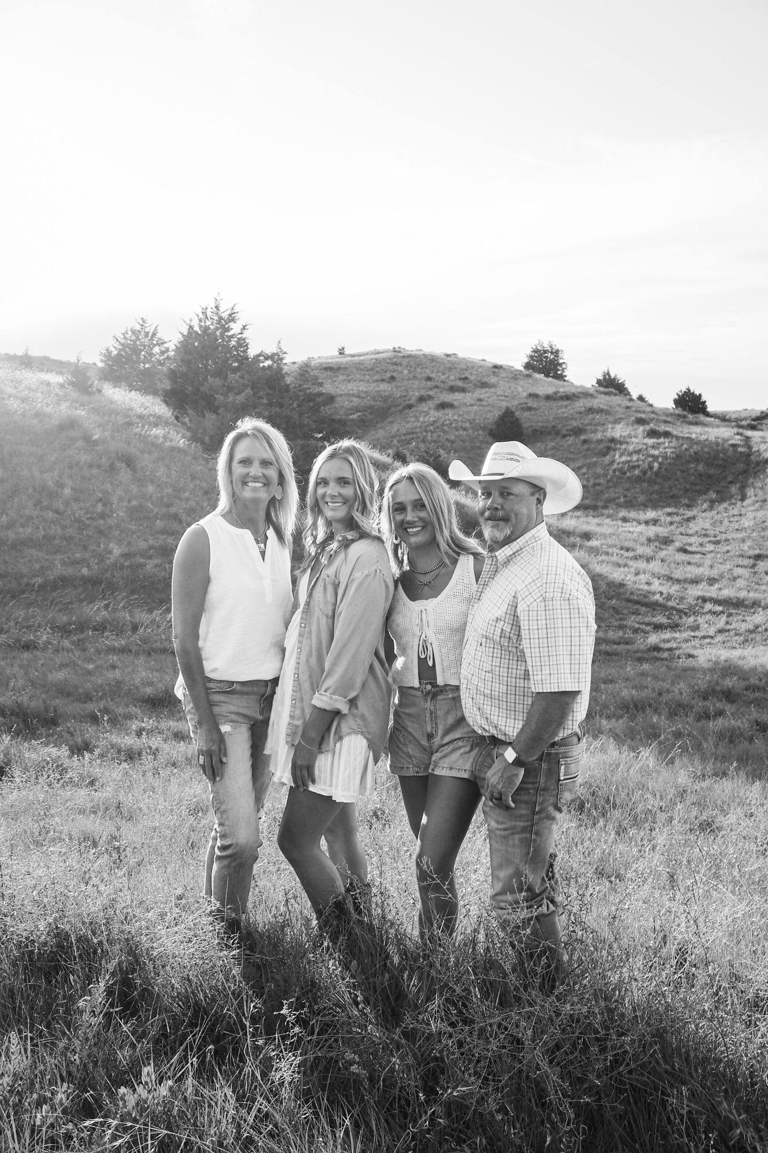 Black and white photo of four smiling people posing in a grassy field, one man wearing a cowboy hat.