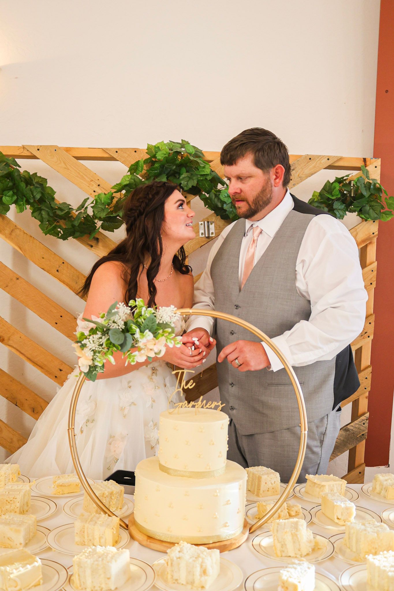 A bride and groom share a tender moment while cutting their two-tier white wedding cake at reception.