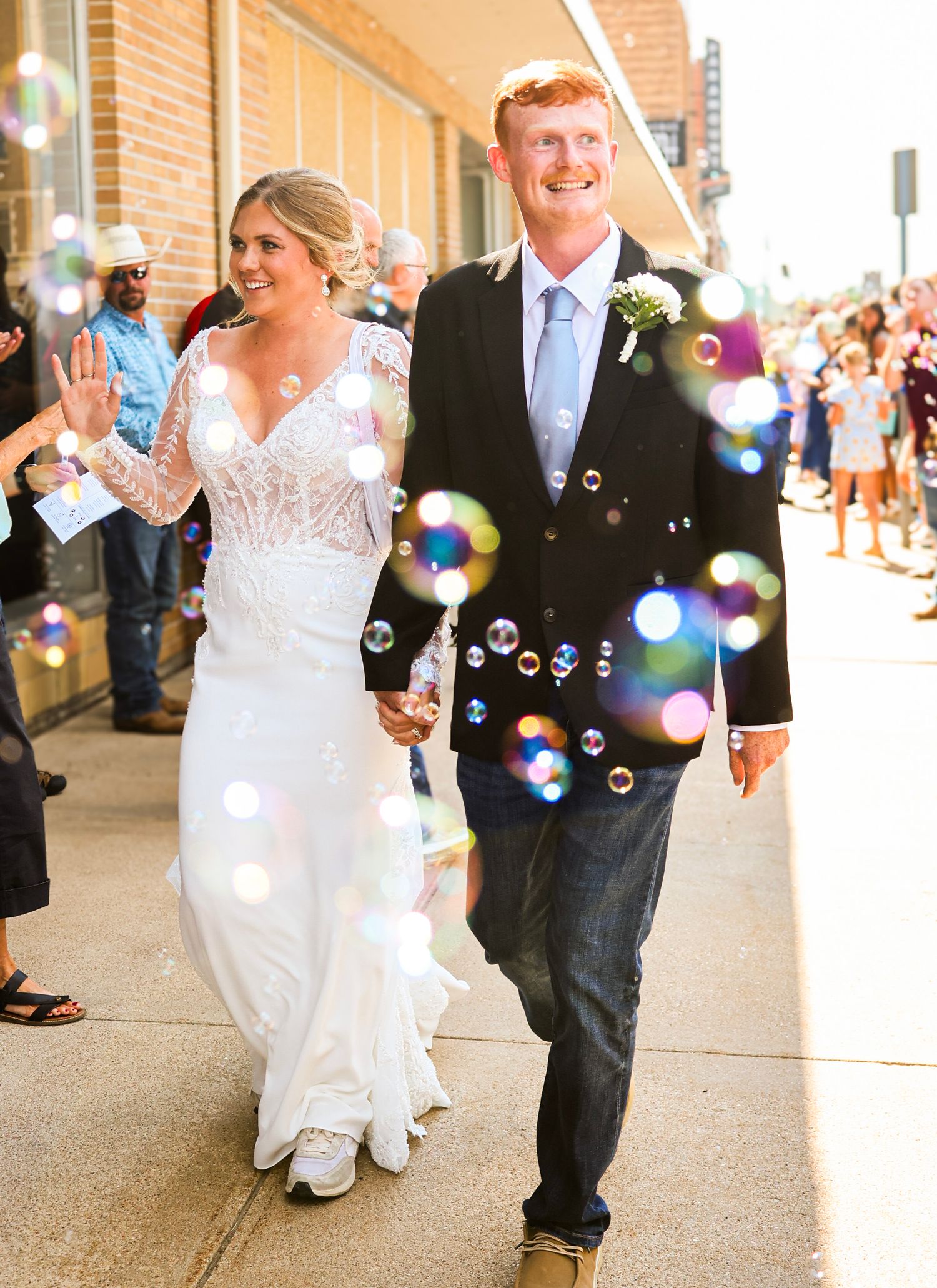 Bride and groom walk through bubble send-off after wedding ceremony on a sunny downtown sidewalk.