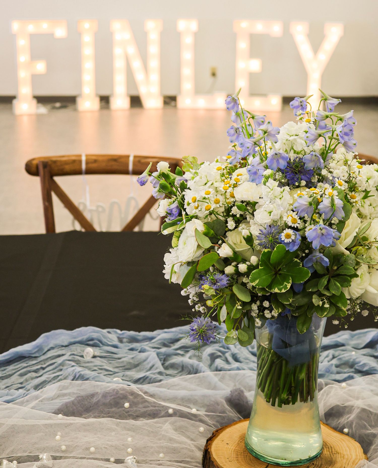 Blue and white wildflower bouquet in glass vase with illuminated FINLEY marquee letters in background.