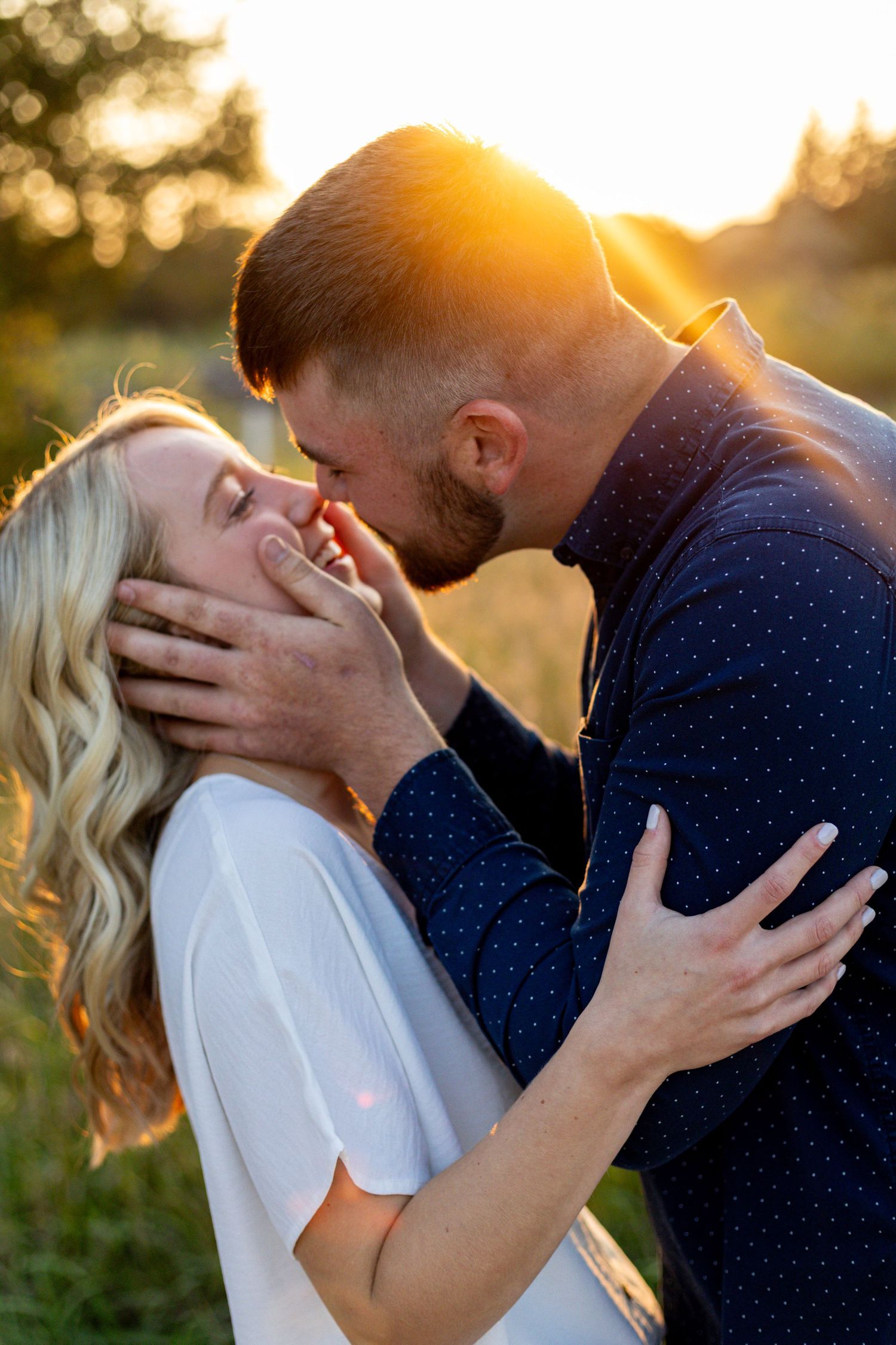 Couple sharing romantic sunset kiss in golden hour light in an open field.