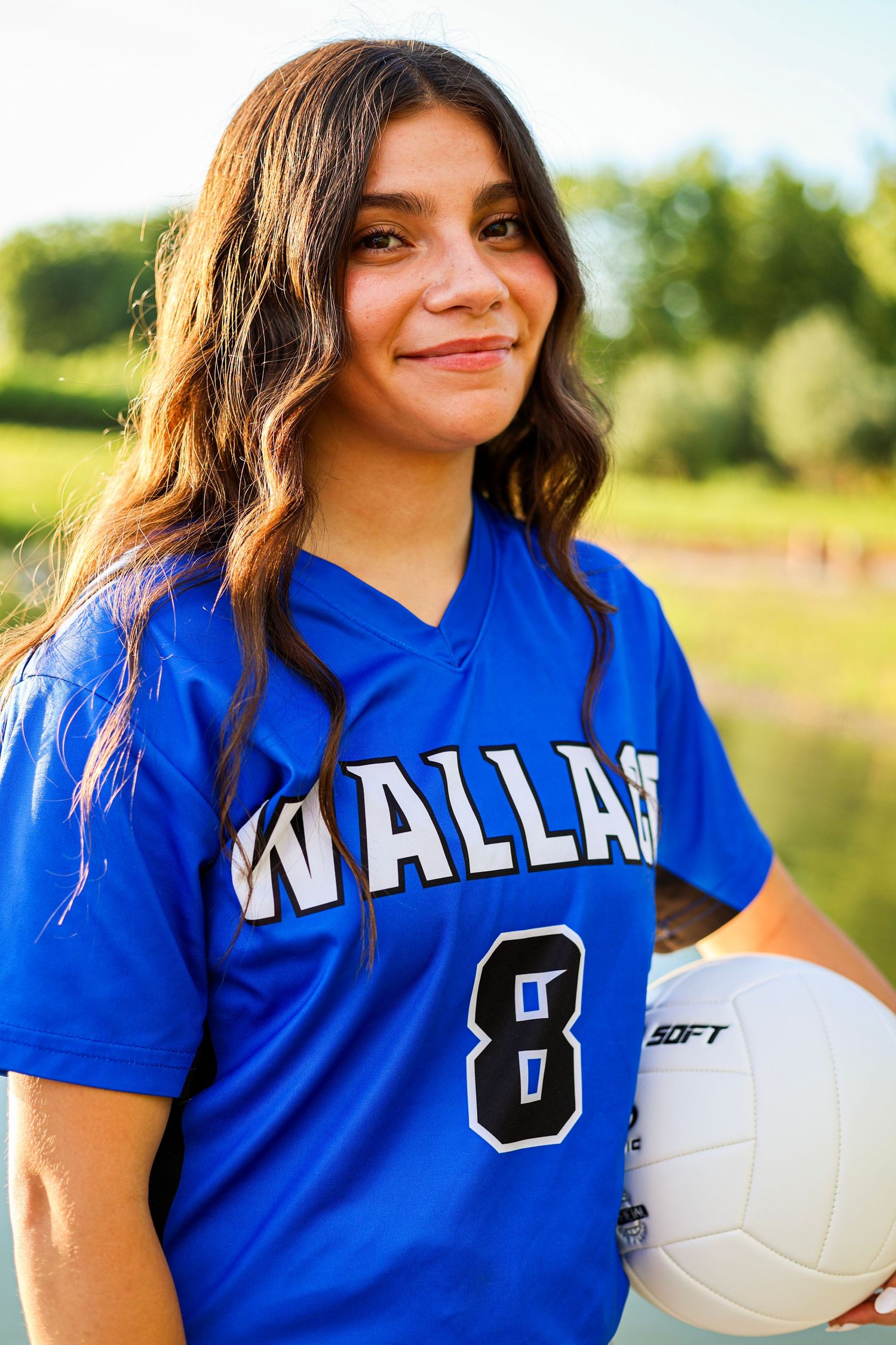 Close-up portrait of young female athlete in blue Wallace number 8 volleyball jersey holding ball outdoors.