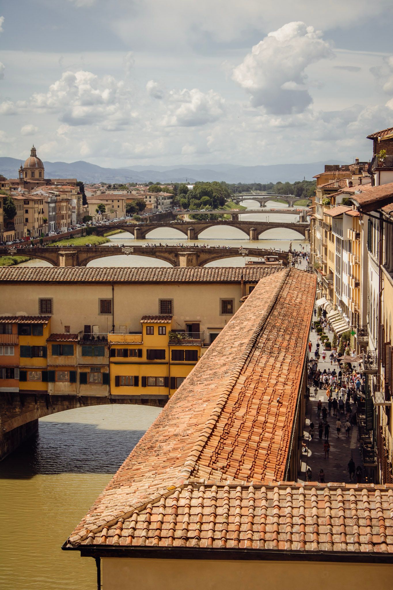 Aerial view of Ponte Vecchio bridge over Arno River in Florence, Italy, with terracotta rooftops and historic buildings.