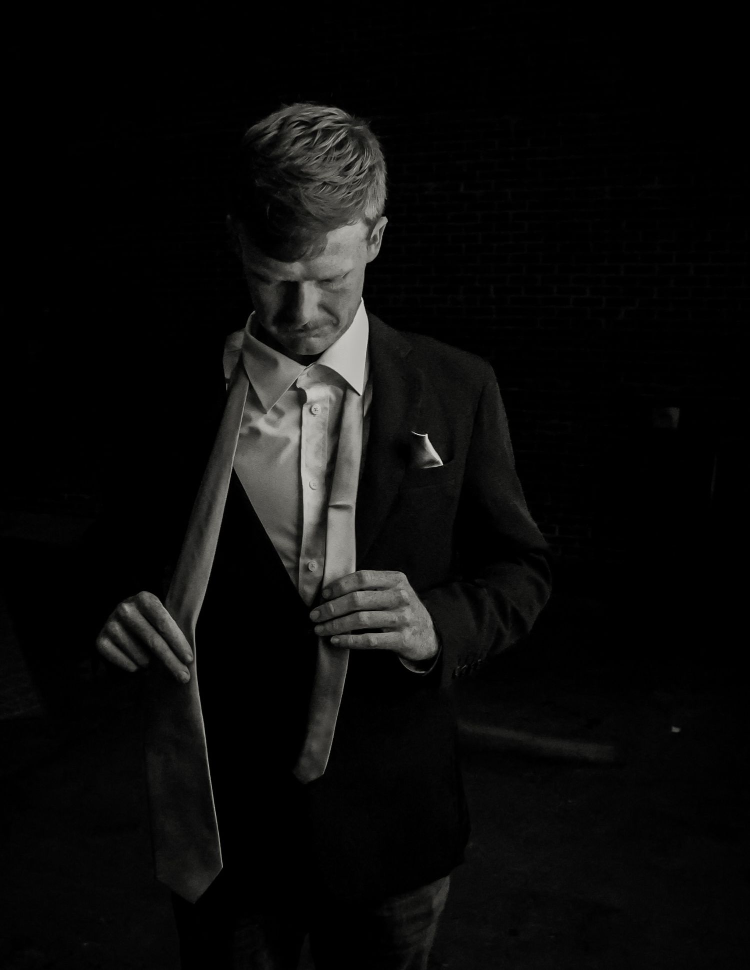 Black and white portrait of a groom adjusting his tie while wearing a formal suit with boutonniere.