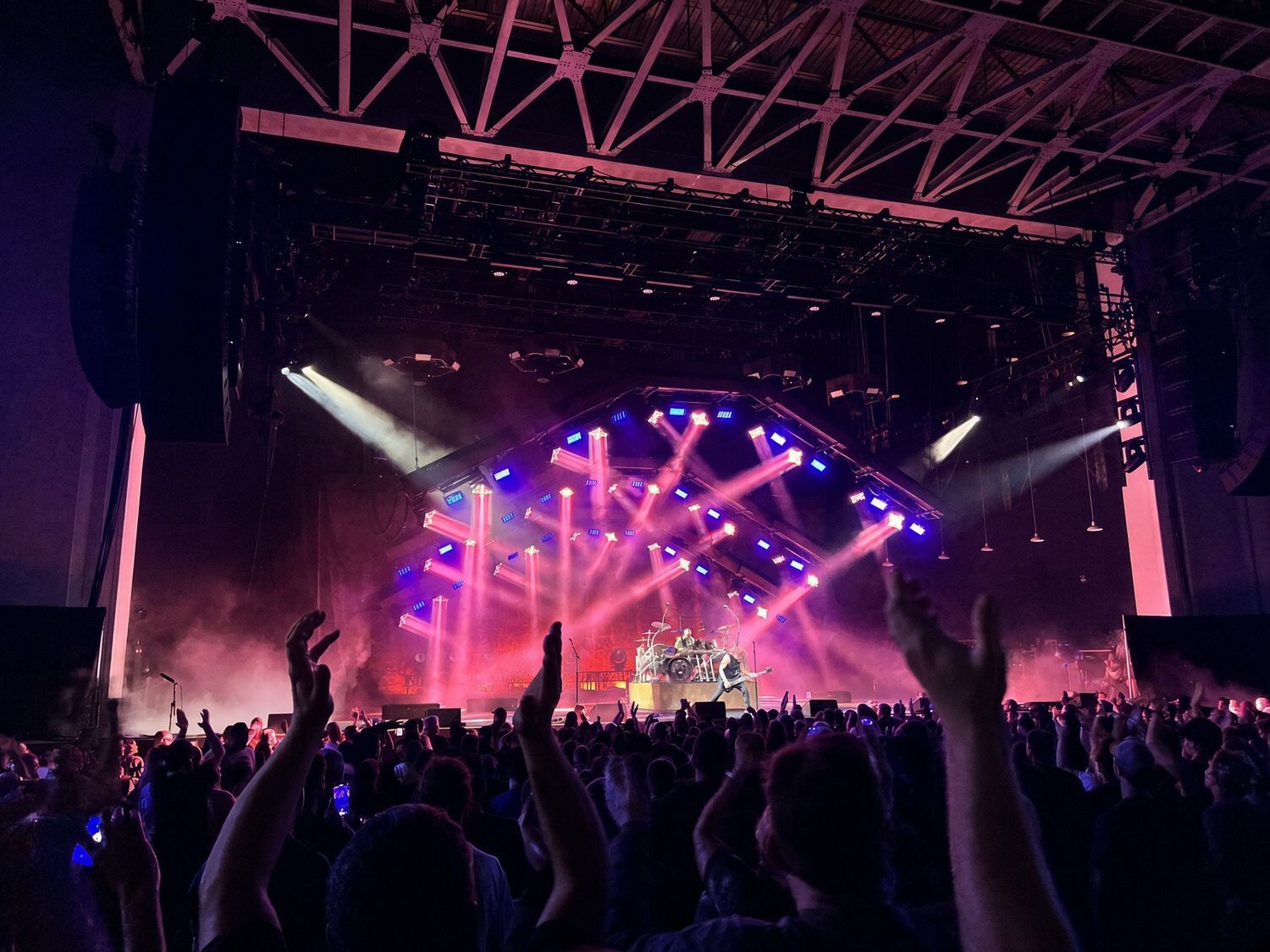 Energetic concert crowd with raised hands under vibrant purple stage lights at a live music event.