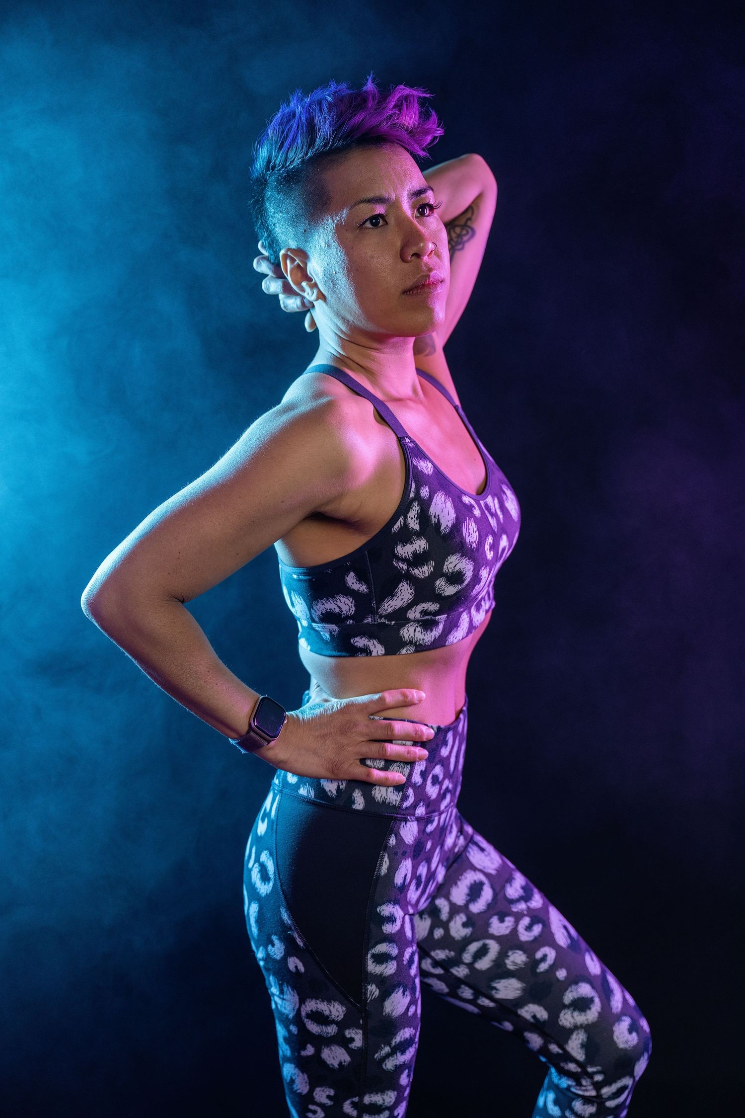Muscular woman in leopard print athletic wear poses confidently under blue and purple neon lights against dark background.