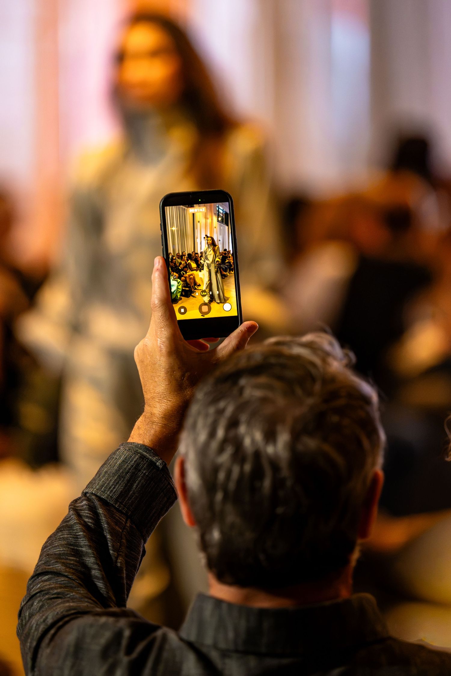 Audience member photographing a runway model on a smartphone at Charlotte Fashion Week.