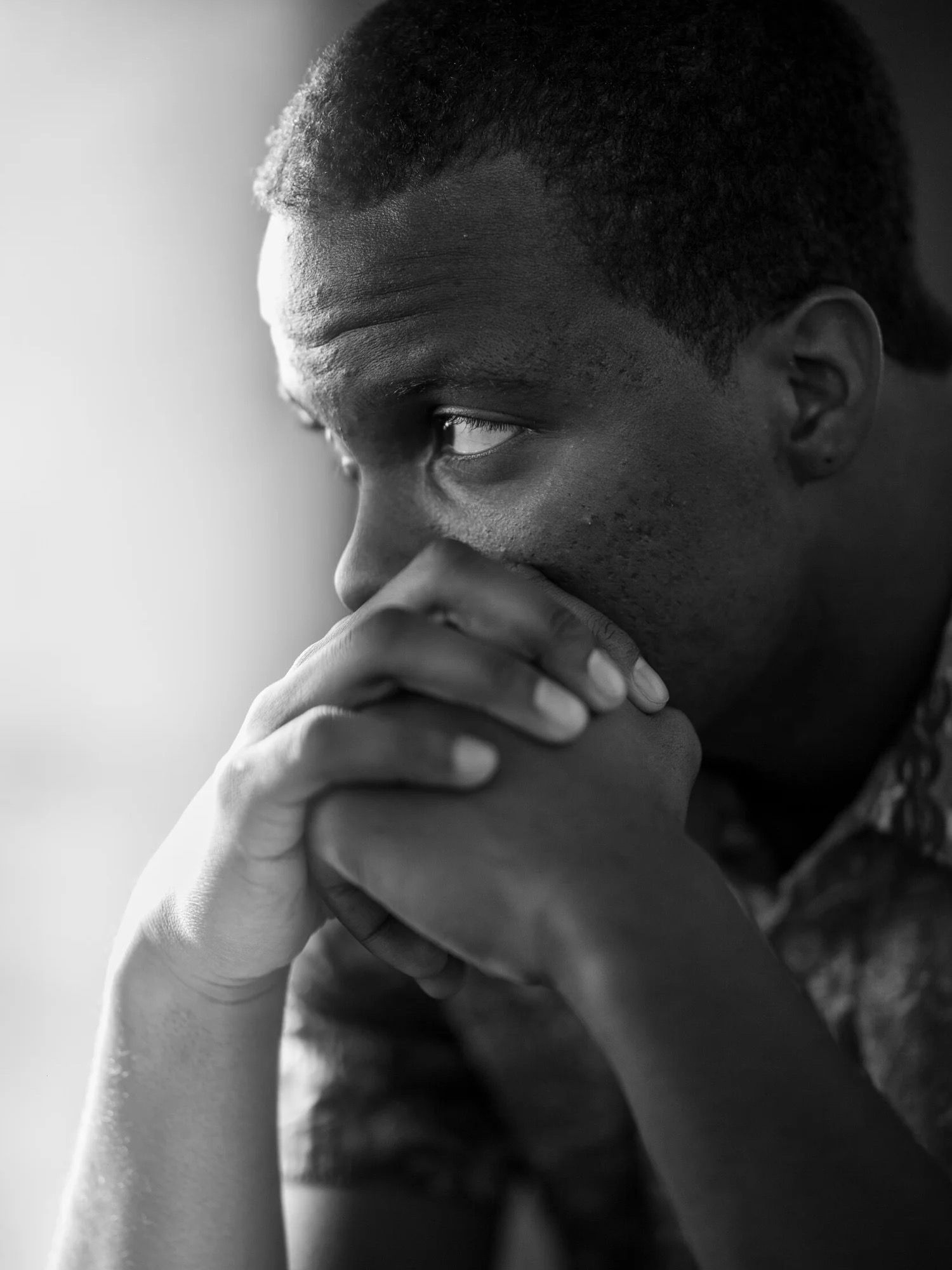 Black and white portrait of a thoughtful man with hands clasped near his face.