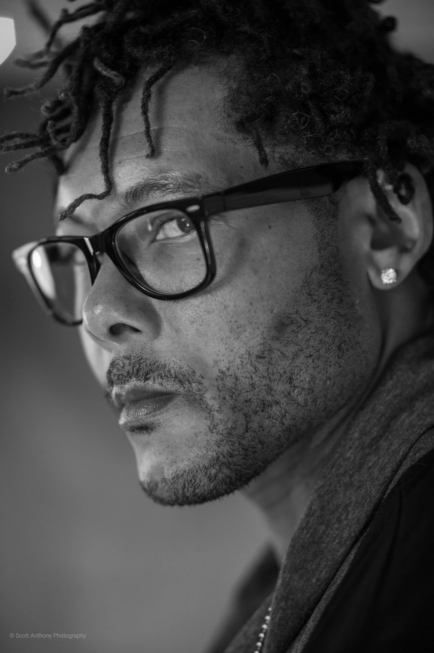 Black and white close-up portrait of a man with dreadlocks wearing black glasses.