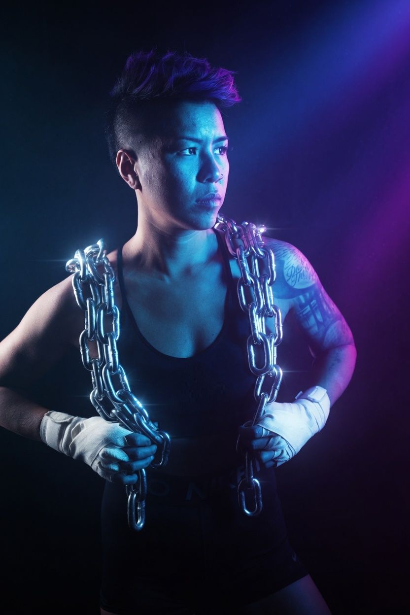 Muscular person holding metal chains under dramatic blue and purple lighting, wearing a black tank top and white hand wraps.
