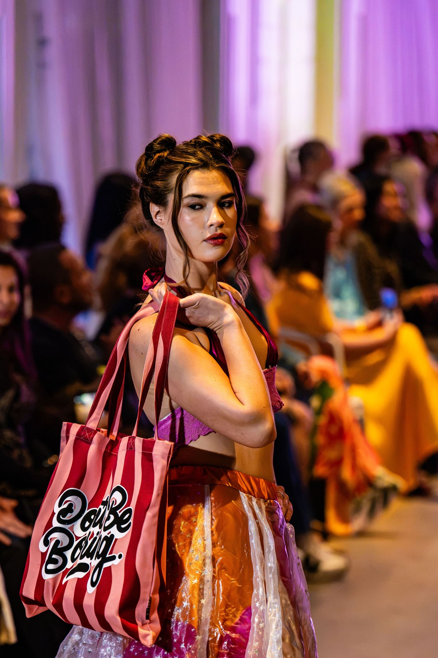 Model carrying a red striped tote and wearing a colorful layered outfit on the Charlotte Fashion Week runway.