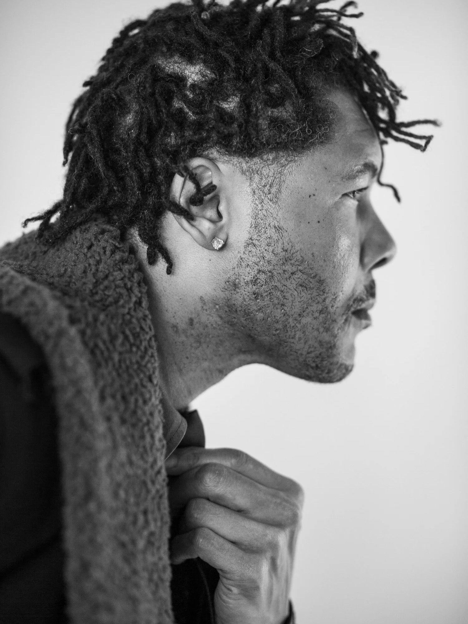 Black and white side profile portrait of a man with dreadlocks and an earring.