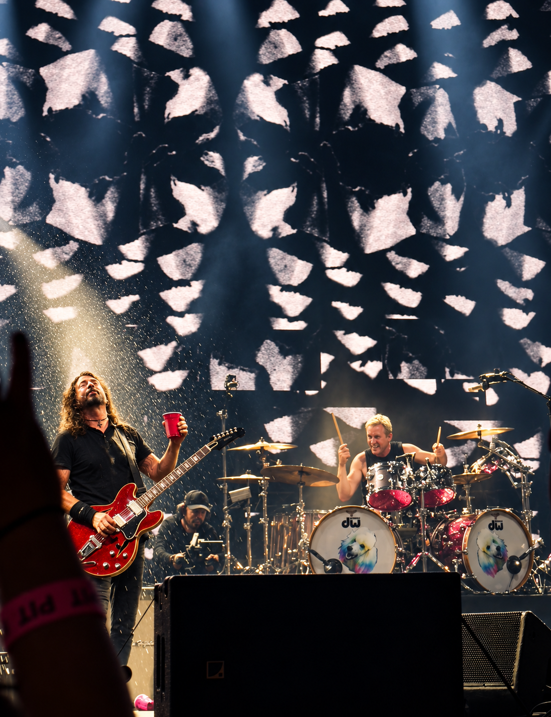 Rock band performs live on stage with dramatic lighting, guitarist singing and drummer playing behind a DW drum kit.