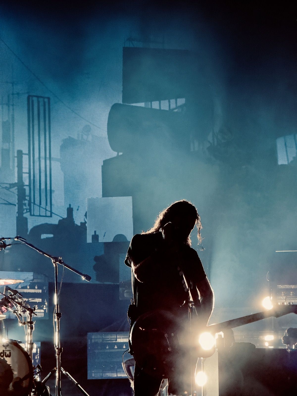 Silhouetted rock guitarist performing on a dramatic foggy stage with blue lighting and concert equipment backdrop.