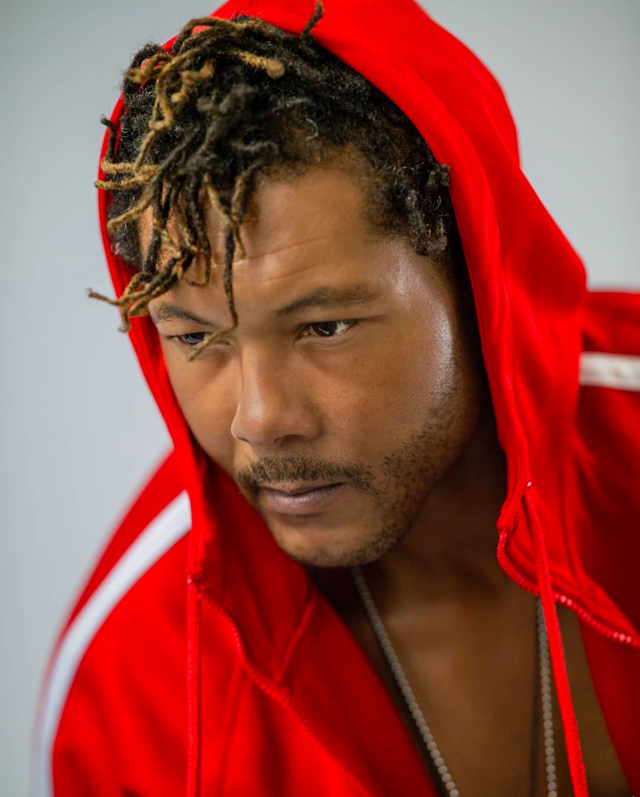 Man with dreadlocks wearing red hoodie with serious expression in close-up portrait.