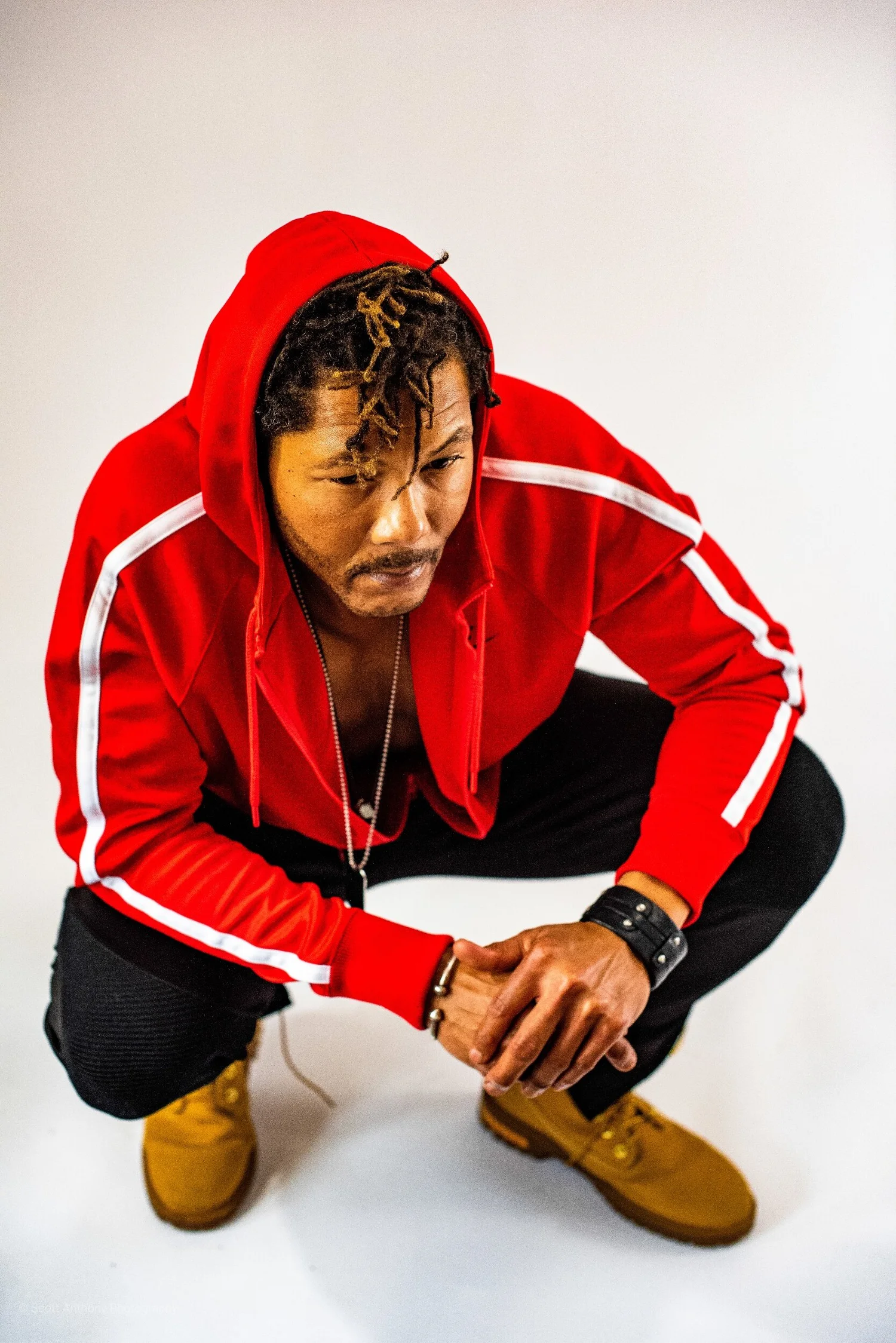 Man in red hoodie and yellow boots crouching confidently against white background.