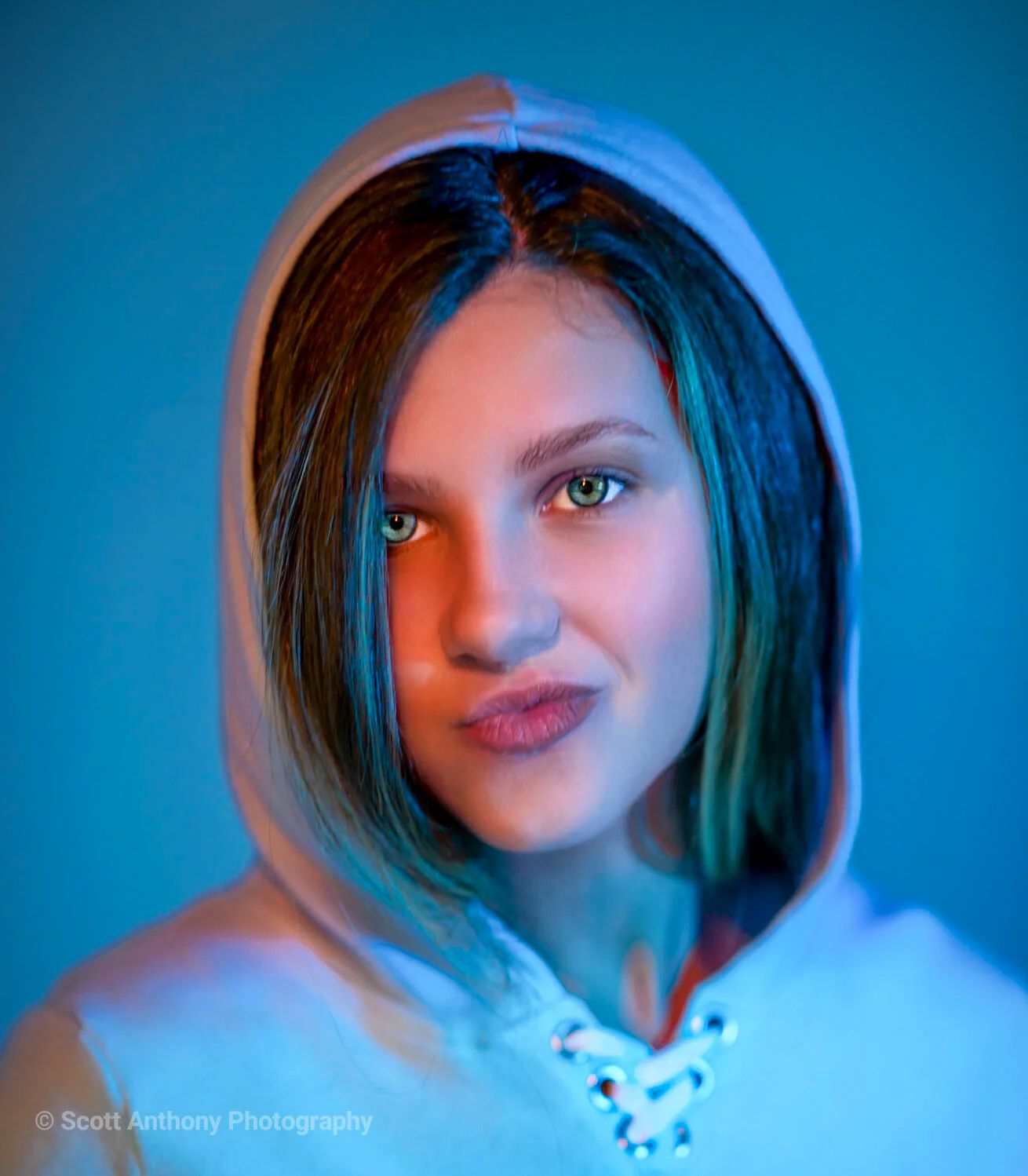 Young woman in a white hoodie photographed under dramatic blue and orange lighting.