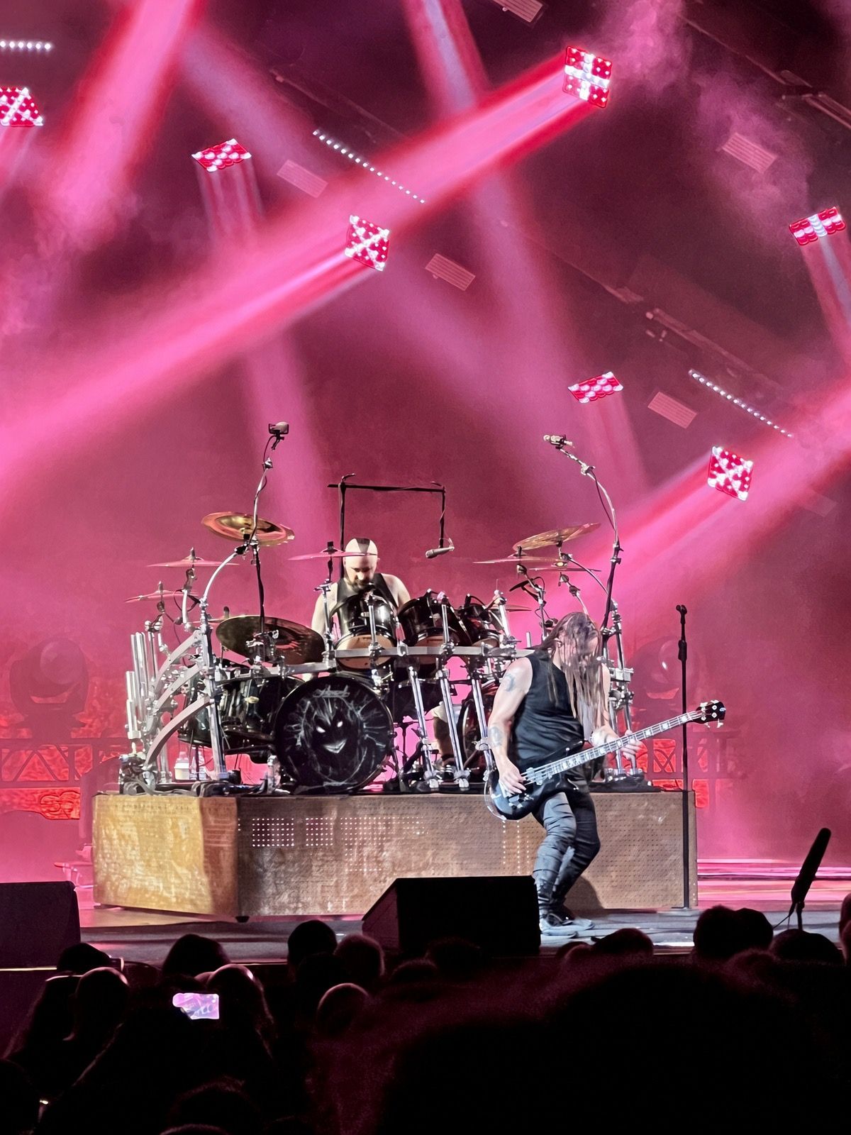 Rock band performs on stage with dramatic pink and red lighting beams during an energetic live concert.