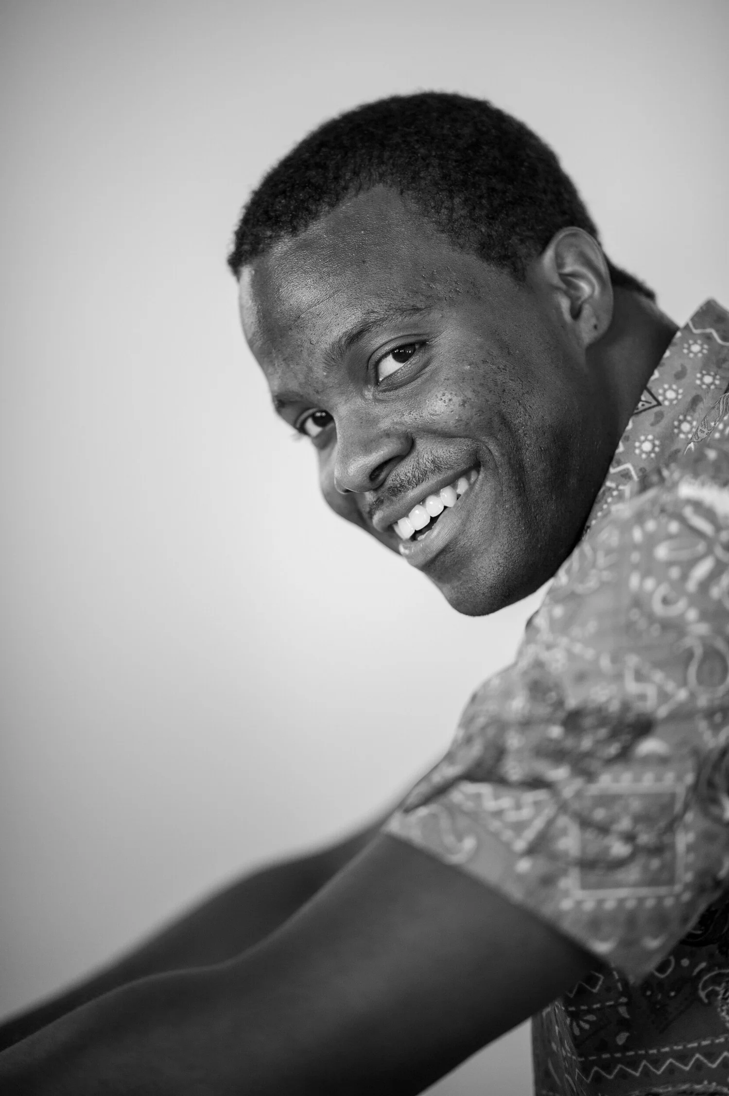 Black and white portrait of a smiling man in a patterned shirt.