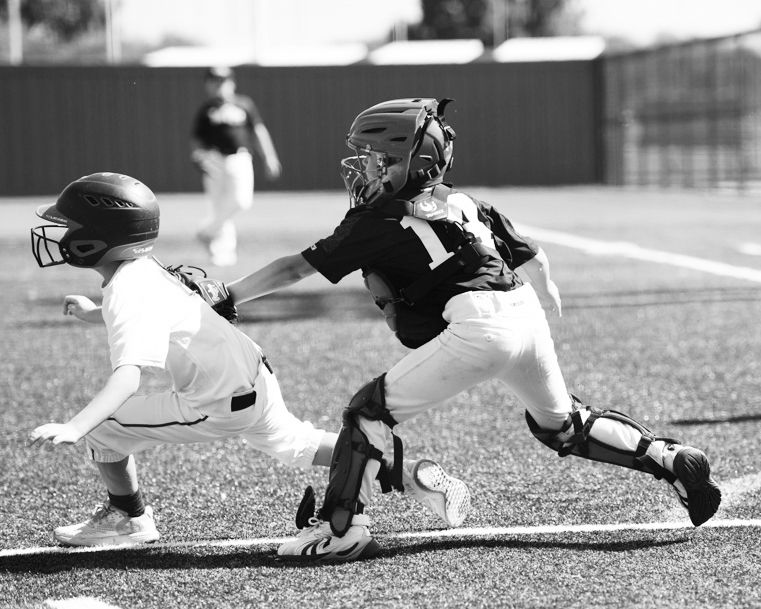 Youth baseball catcher tags out a runner caught between 3rd base and home plate during a little league game.