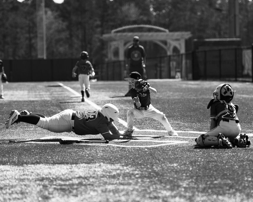 Black and white photo of baseball player sliding into home plate as catcher attempts tag during game.