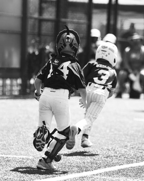 Youth baseball catcher attempts to run down and tag out a runner caught between 3rd base and home plate.
