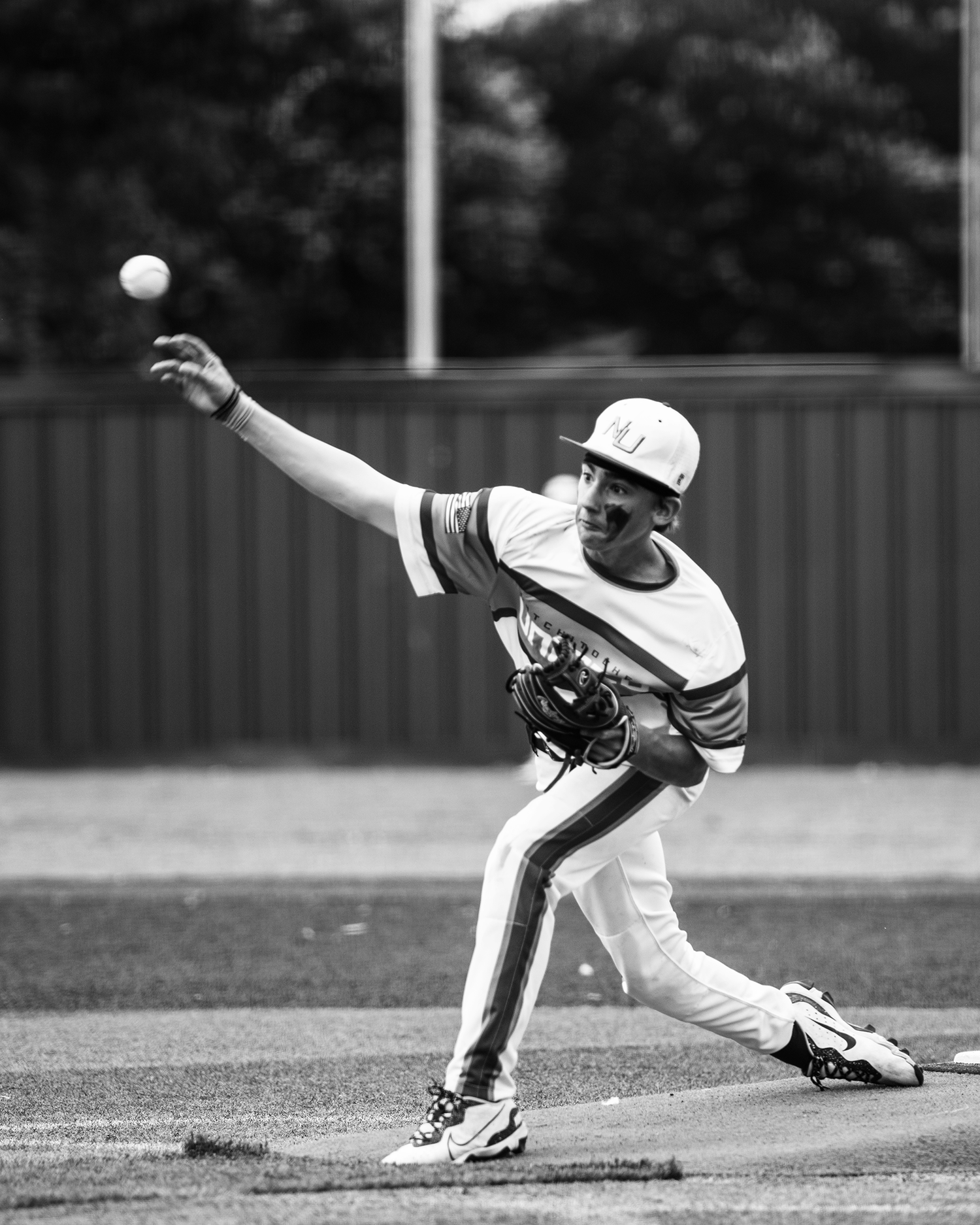 Black and white photo of a baseball pitcher in mid-throw, wearing a cap and uniform on a baseball field.