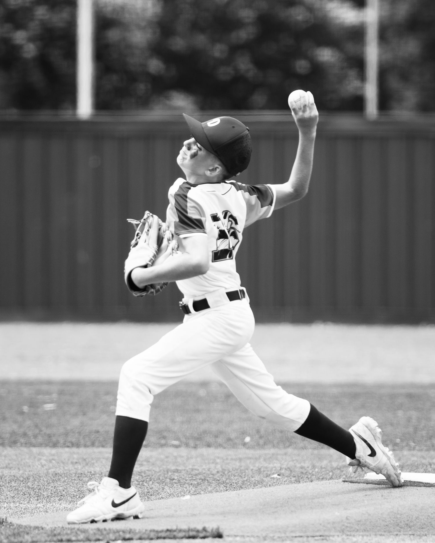 Young baseball pitcher in white uniform mid pitch, black and white action photo on the mound.