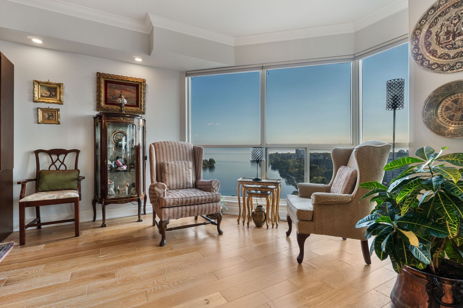 Elegant living room with hardwood floors, two wingback chairs, and floor-to-ceiling windows showcasing stunning waterfront views.