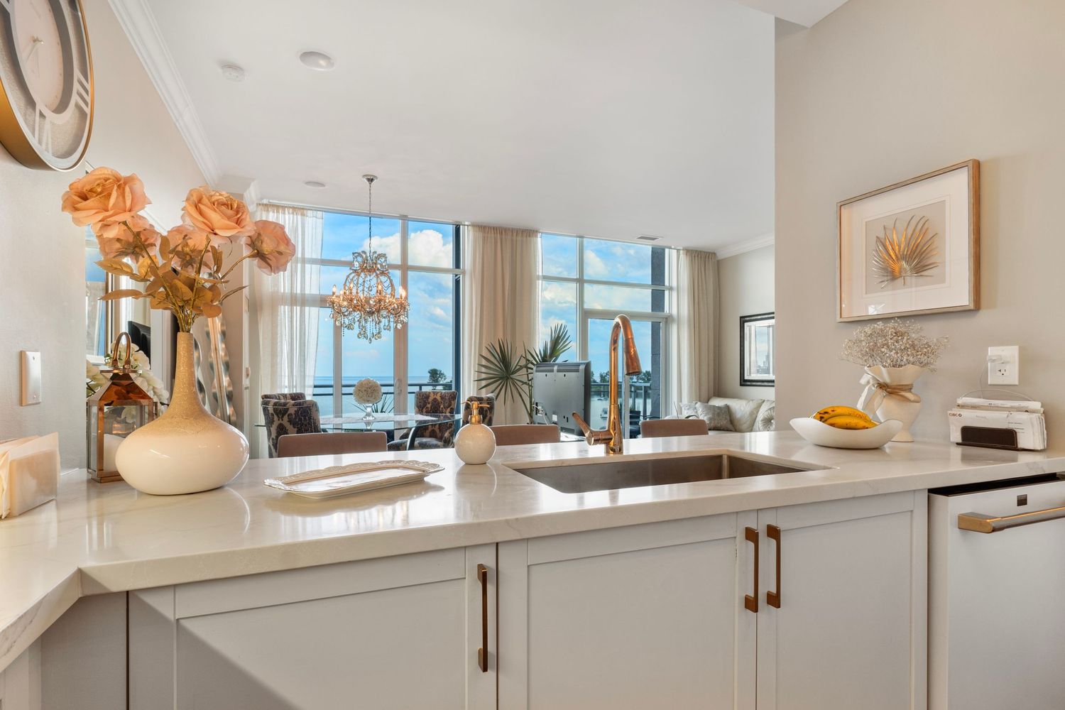 Modern kitchen with white cabinets, quartz countertops, and a large window overlooking a scenic waterfront view.
