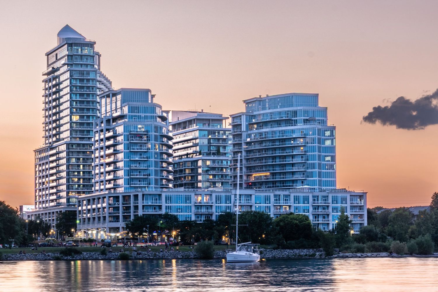 Modern luxury waterfront condominiums reflecting sunset light, with a marina and calm waters in the foreground.