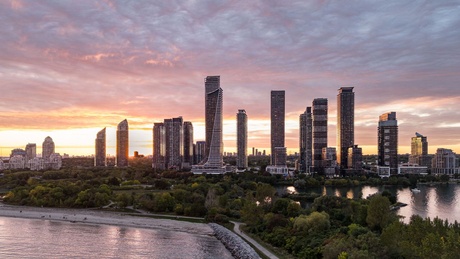 Stunning sunset skyline view of modern skyscrapers along a waterfront with colorful pink and purple clouds.