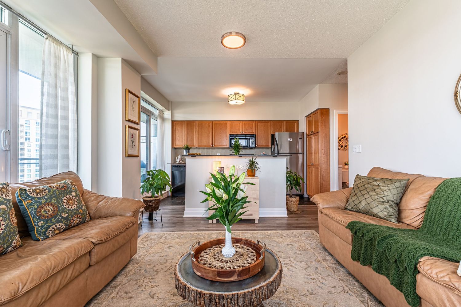 Open-concept living room with leather sofas, wood coffee table, and adjoining kitchen with warm cabinetry.