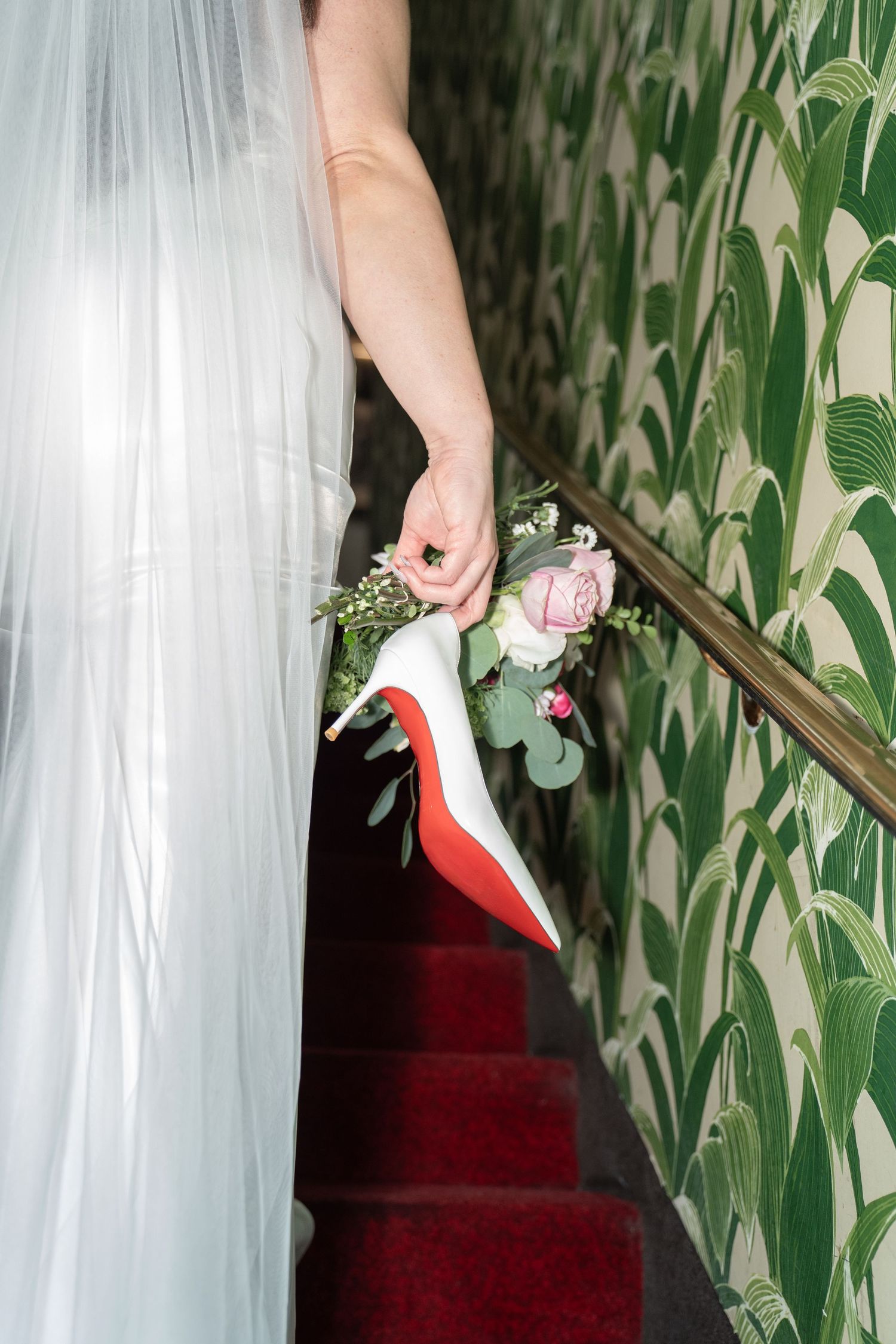 Bride descends red carpeted staircase holding bouquet and red-soled Christian Louboutin heels. Las Vegas elopement photographer.