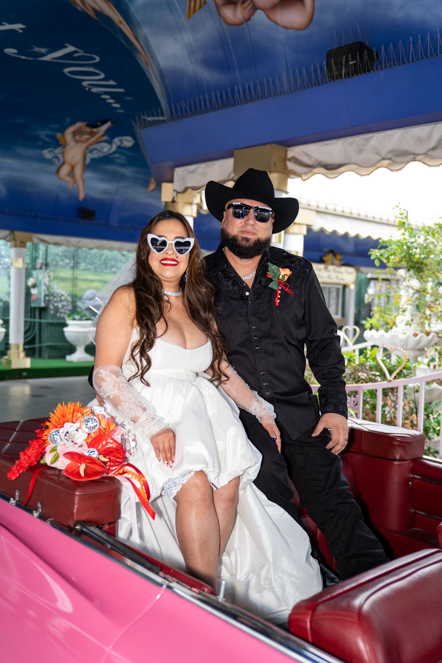 Bride and groom in cowboy hat sit in a pink convertible at a Las Vegas drive-through wedding chapel. Las Vegas elopement photographer