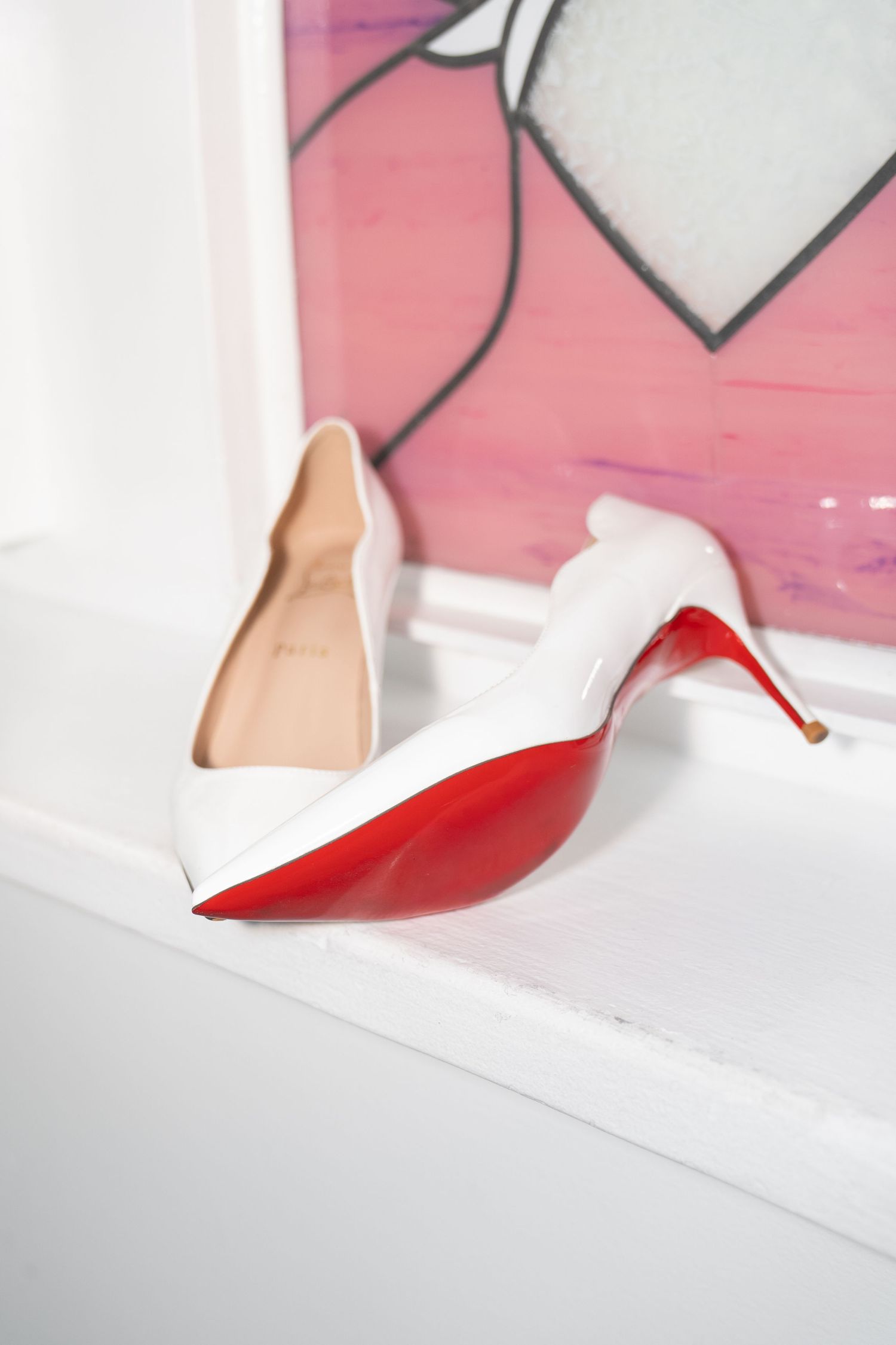 White Christian Louboutin stiletto heels with red soles displayed on windowsill with heart stained glass. Las Vegas elopement photographer
