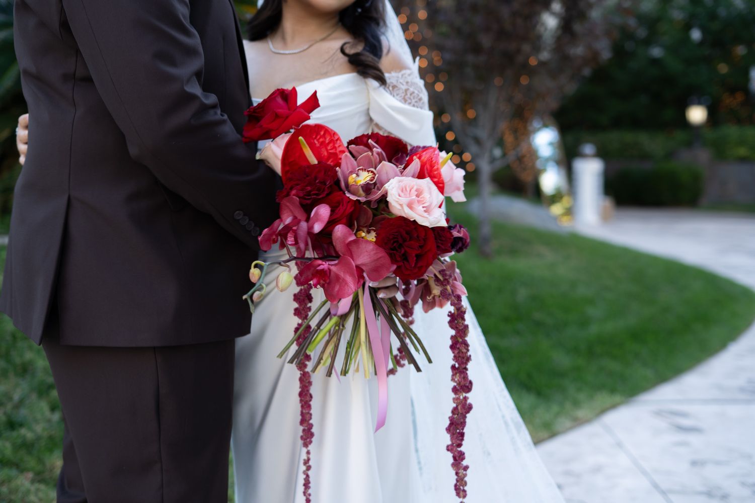 Close-up of bride and groom holding cascading red and burgundy wedding bouquet with pink roses outdoors. Las Vegas wedding photographer
