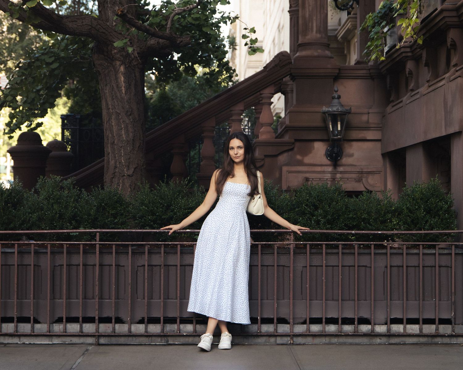 Full-length portrait of a woman leaning against an iron fence outside an Upper East Side brownstone.