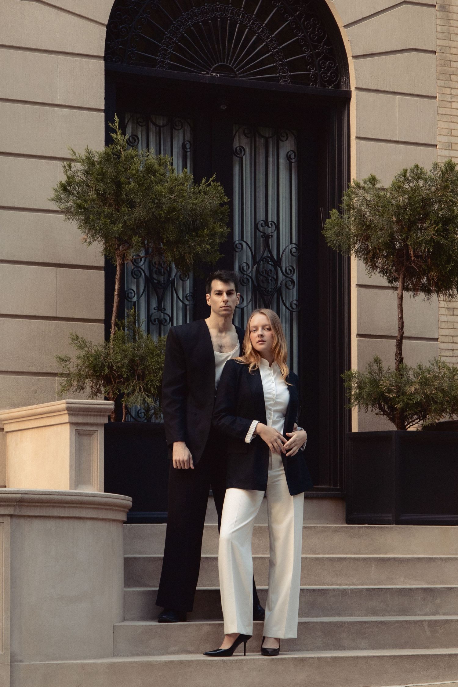 Vin and Regina pose together on townhouse steps beneath a tall arched iron doorway flanked by potted trees.