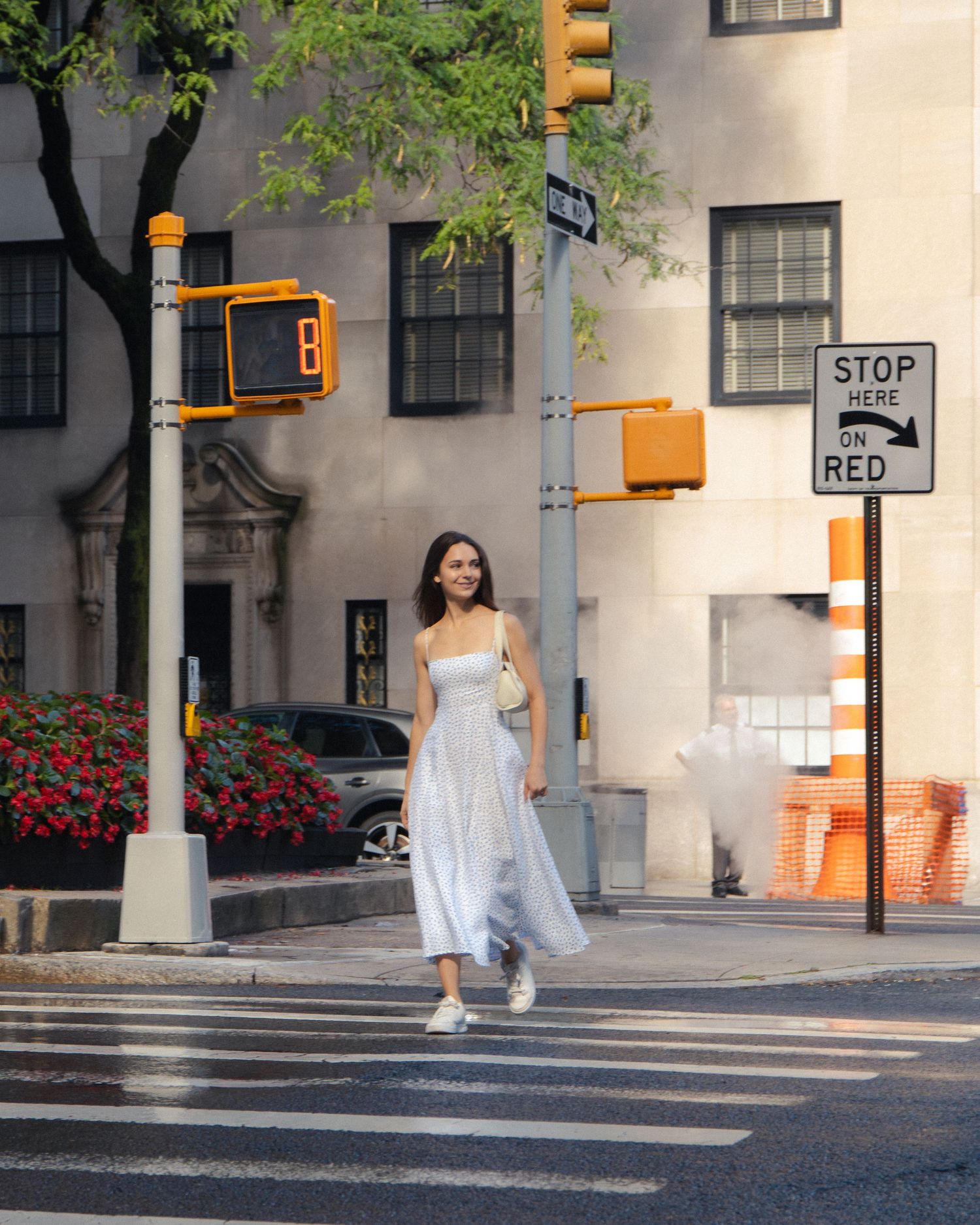 Woman crossing a New York City street beneath yellow traffic lights, with steam rising behind her.