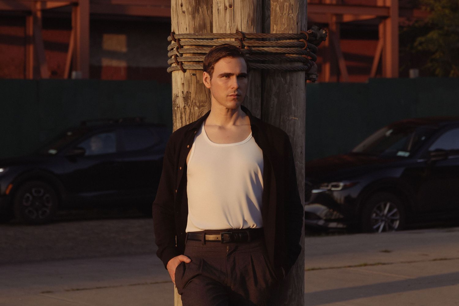 Dylan leans against a rope-wrapped wooden post as warm evening sunlight cuts across the industrial street behind him.