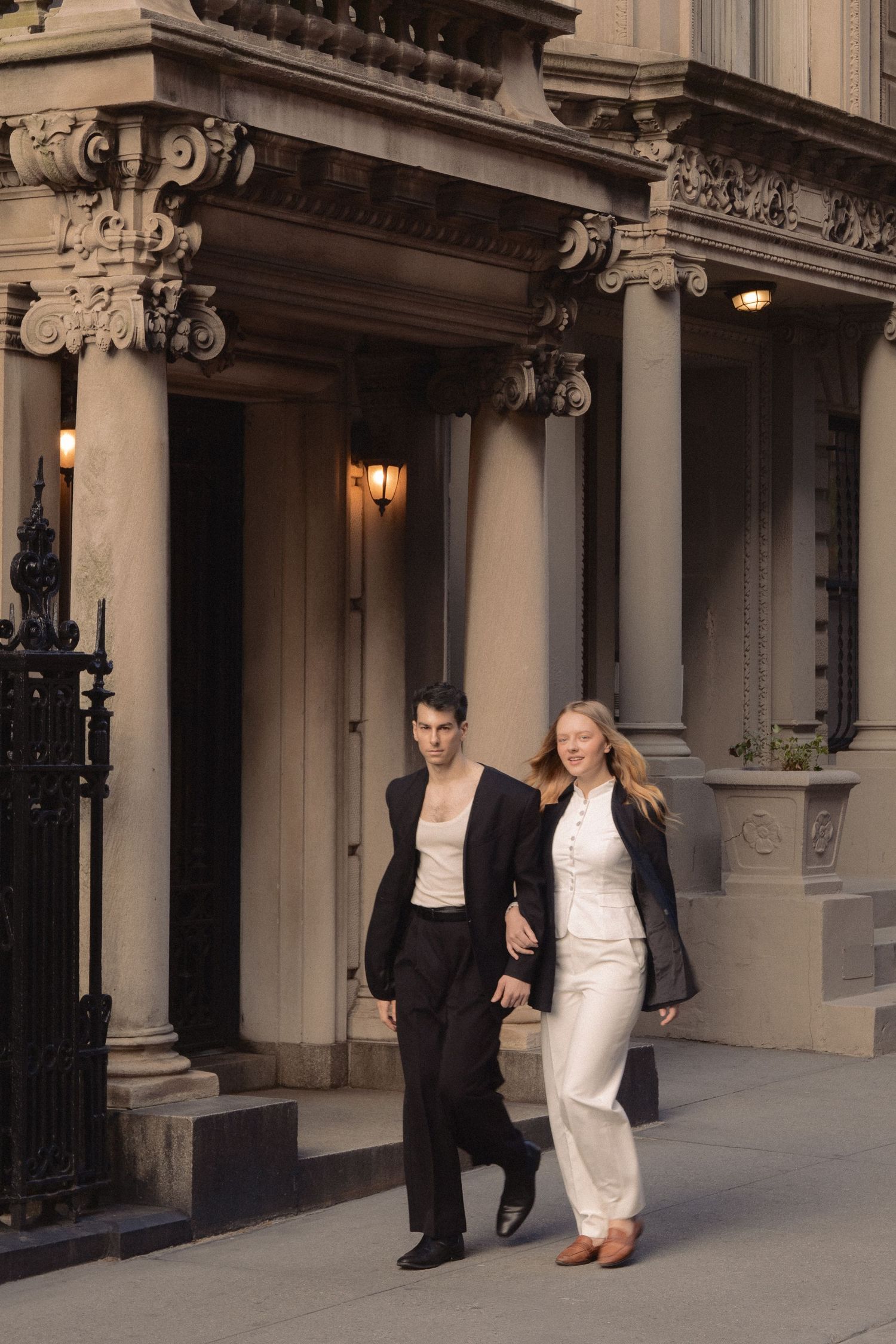 Vin and Regina walk arm in arm past carved columns and wrought-iron railings outside an Upper West Side townhouse.