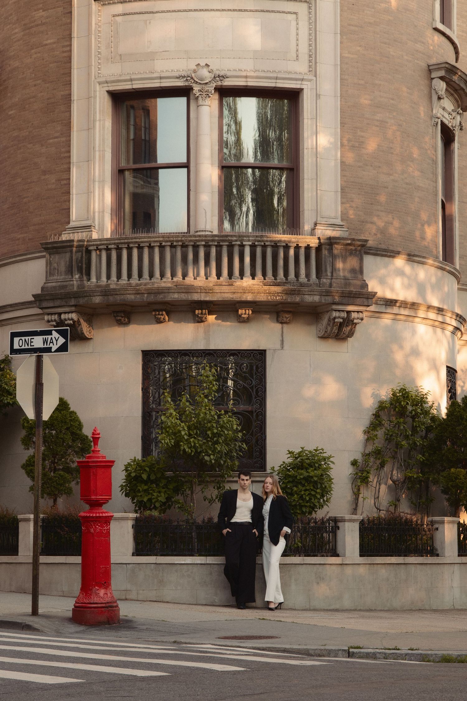 Vin and Regina pose at the base of a grand corner townhouse beside a red fire alarm box on the Upper West Side.
