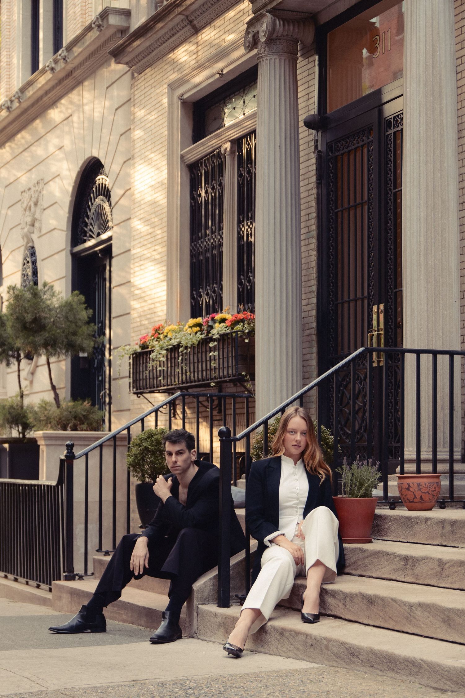 Vin and Regina sit on opposite sides of an iron railing on a townhouse stoop framed by ornate columns.