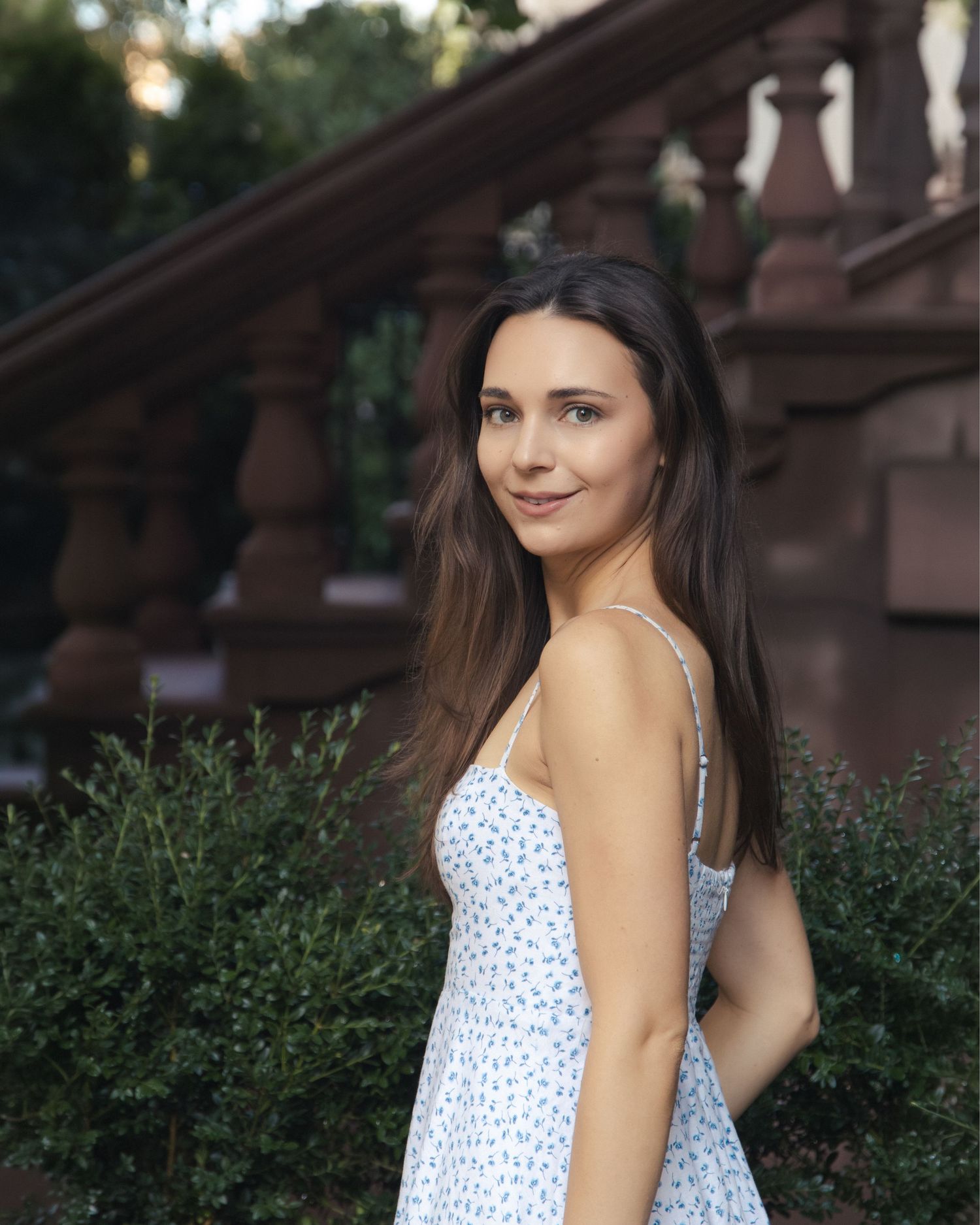 Close-up portrait of Anastasia looking over her shoulder beside brownstone steps and green shrubs.