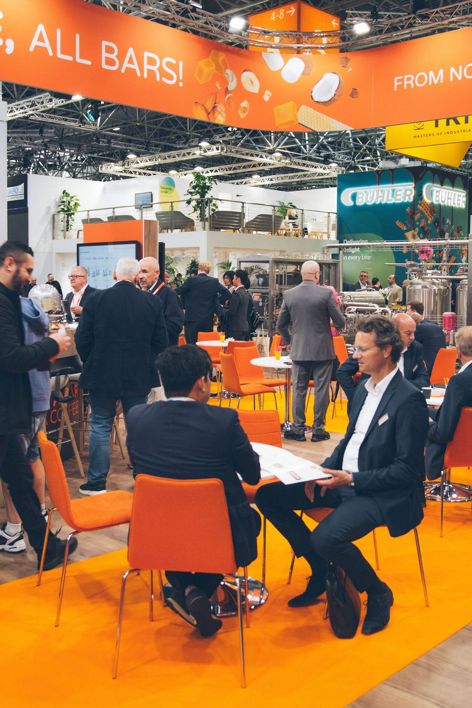 Business professionals network and meet at a vibrant orange trade show exhibition booth with orange chairs.