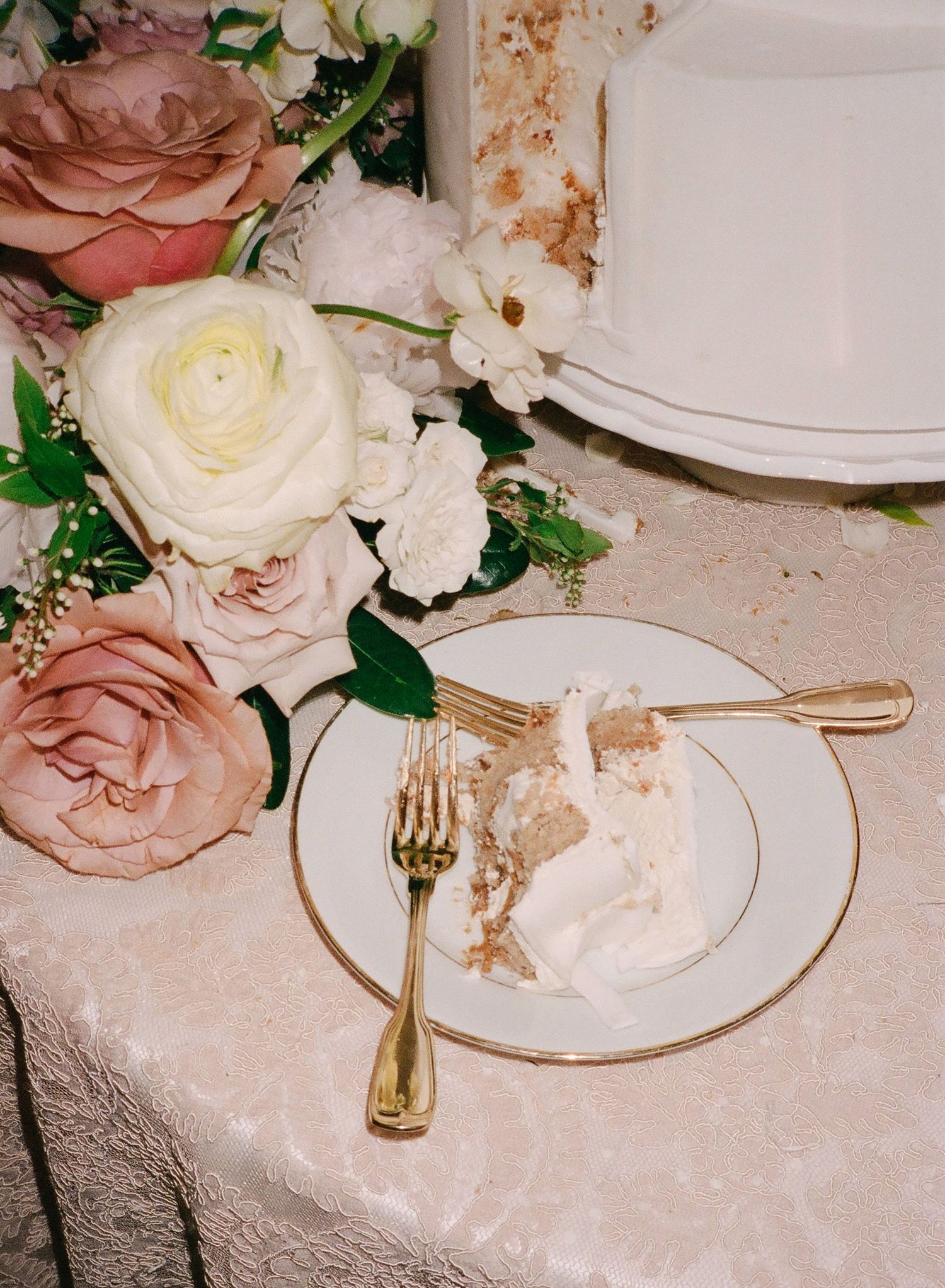 Elegant table setting with pink roses, white ranunculus flowers, gold cutlery, and white plates on a textured tablecloth.
