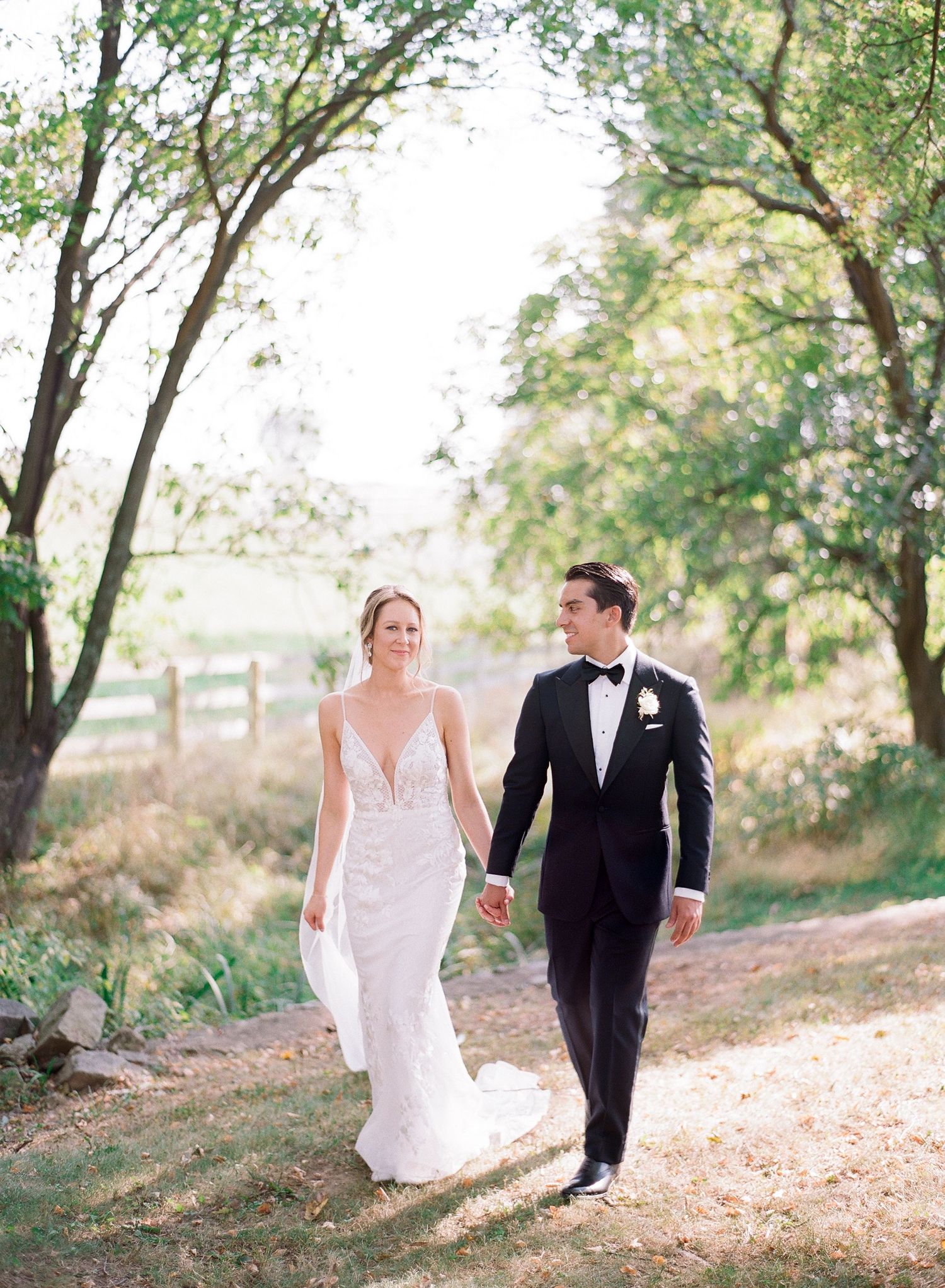 A couple in wedding attire walking together along a tree-lined path on their special day.