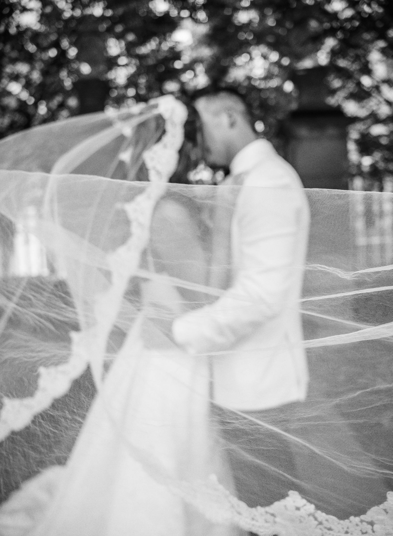 A flowing white veil catches the breeze during an outdoor wedding photoshoot, creating an ethereal effect.