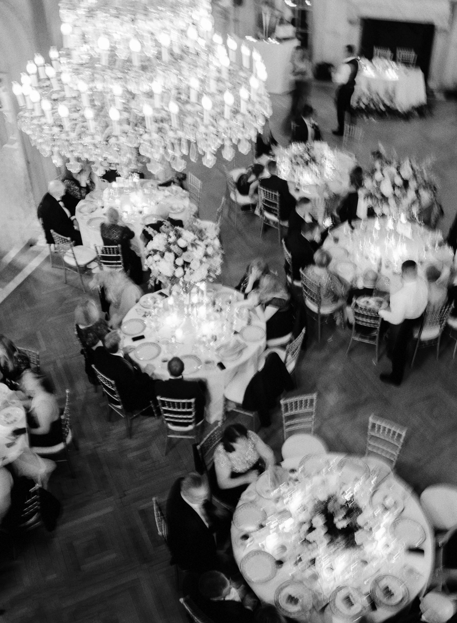 Black and white aerial view of a formal event with multiple round tables and guests seated in an elegant reception space.